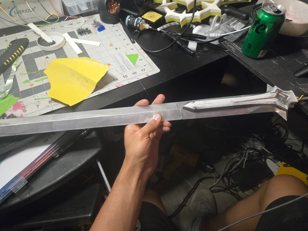 Sword blade on the workbench after sanding reset, before the panel-wash recovery