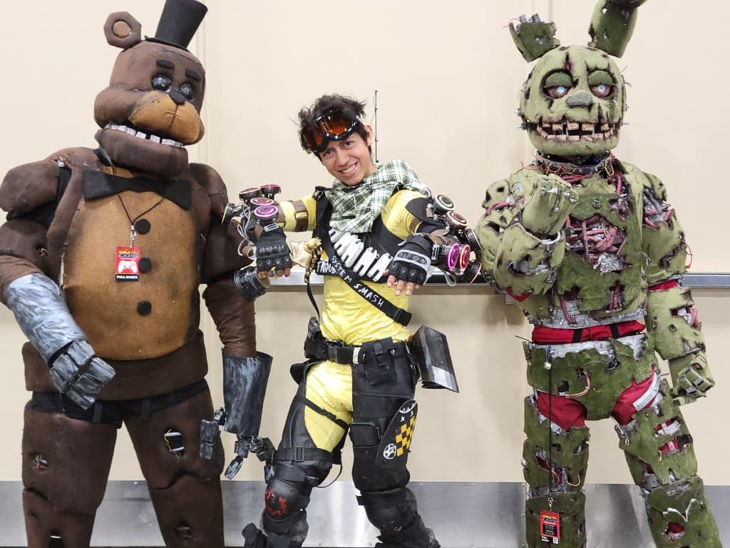 Mirage cosplay at convention with glowing holo gauntlets, alongside Freddy and Springtrap builds